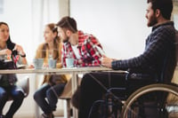 Coworker on wheelchair using digital tablet against photo editors in meeting room at creative office